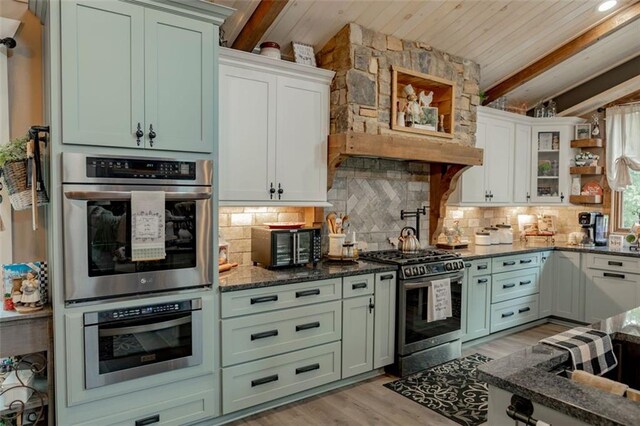 kitchen with white cabinets, backsplash, dark stone counters, light hardwood / wood-style floors, and stainless steel appliances