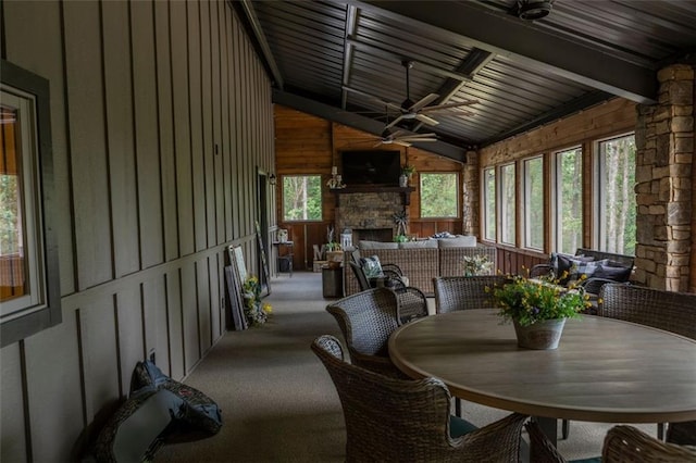 sunroom / solarium with ceiling fan, an outdoor stone fireplace, wooden ceiling, and lofted ceiling with beams