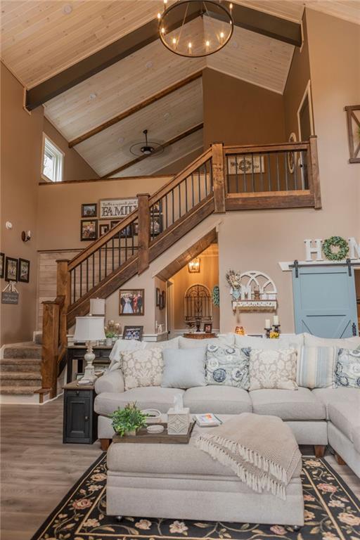 living room with beam ceiling, hardwood / wood-style floors, a barn door, an inviting chandelier, and high vaulted ceiling