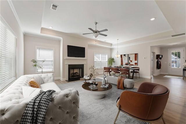 living room with light wood-type flooring, a tray ceiling, visible vents, and crown molding