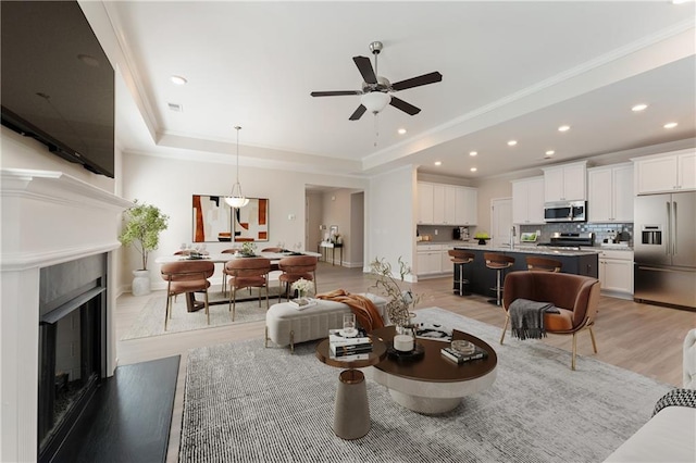 living area with visible vents, light wood-style flooring, a tray ceiling, a fireplace, and recessed lighting