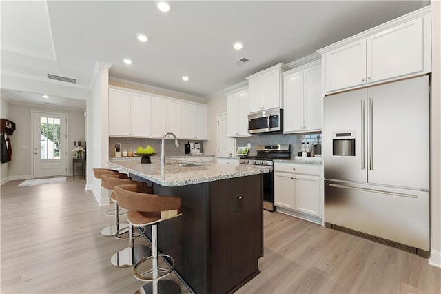 kitchen with light wood finished floors, a breakfast bar area, appliances with stainless steel finishes, crown molding, and a sink