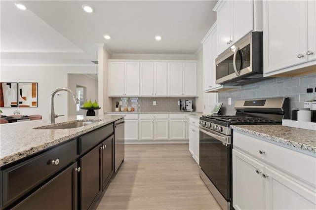 kitchen with light wood finished floors, stainless steel appliances, tasteful backsplash, white cabinets, and a sink