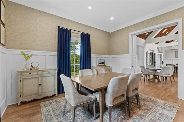 dining area with wainscoting, ornamental molding, light wood-type flooring, and a decorative wall