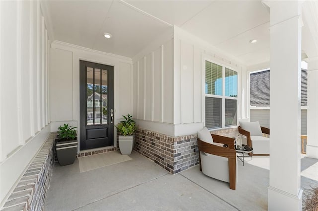 view of exterior entry featuring board and batten siding, covered porch, and brick siding