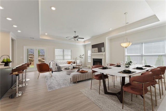 living room featuring a fireplace, crown molding, recessed lighting, a raised ceiling, and light wood-style floors