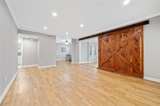 unfurnished living room featuring light wood-type flooring, a barn door, visible vents, and crown molding