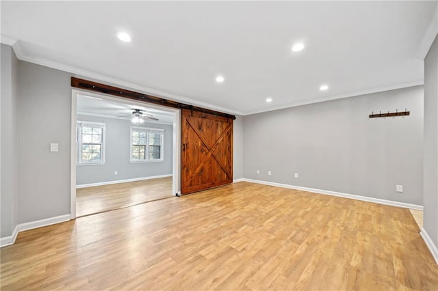 empty room featuring light wood finished floors, a barn door, baseboards, and crown molding