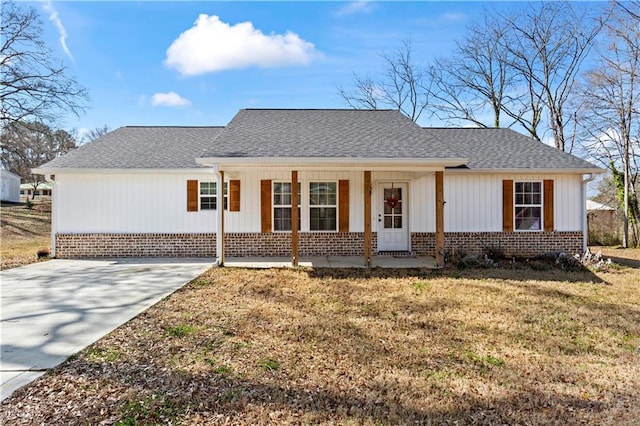 view of front facade with covered porch, roof with shingles, a front lawn, and brick siding