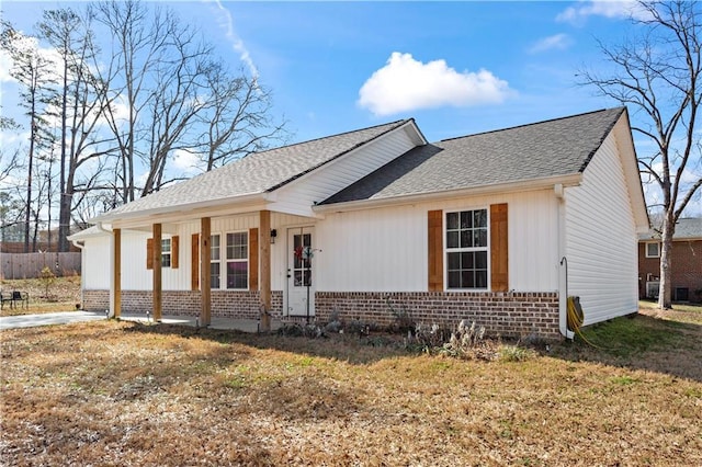 single story home featuring covered porch, brick siding, a front yard, and a shingled roof