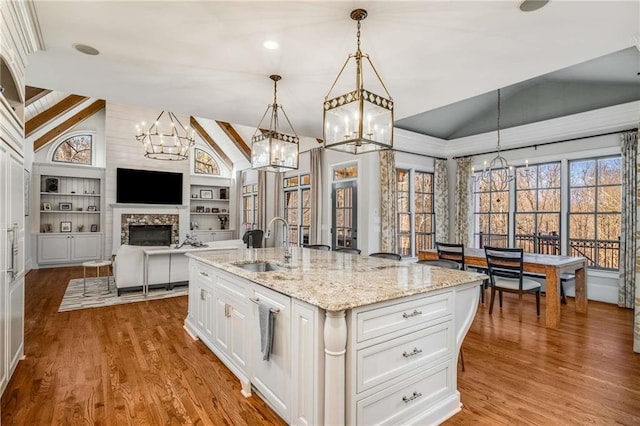 kitchen featuring built in shelves, vaulted ceiling, a fireplace, wood finished floors, and a sink