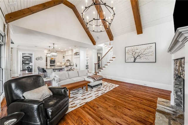 living room featuring beamed ceiling, a notable chandelier, wood finished floors, baseboards, and stairs