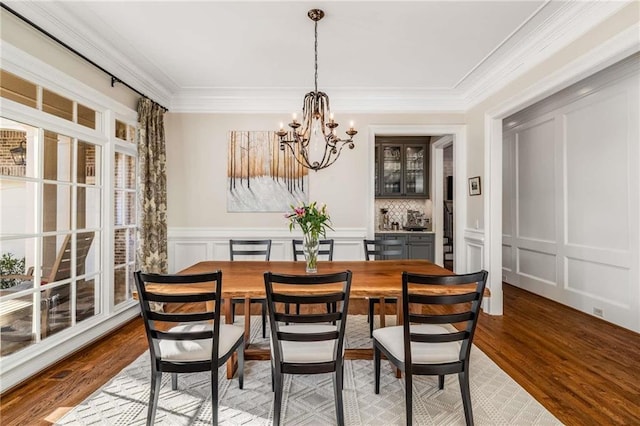 dining room featuring a wainscoted wall, light wood-style floors, an inviting chandelier, crown molding, and a decorative wall