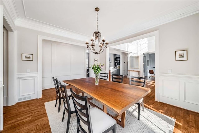 dining space featuring visible vents, crown molding, a decorative wall, and wood finished floors