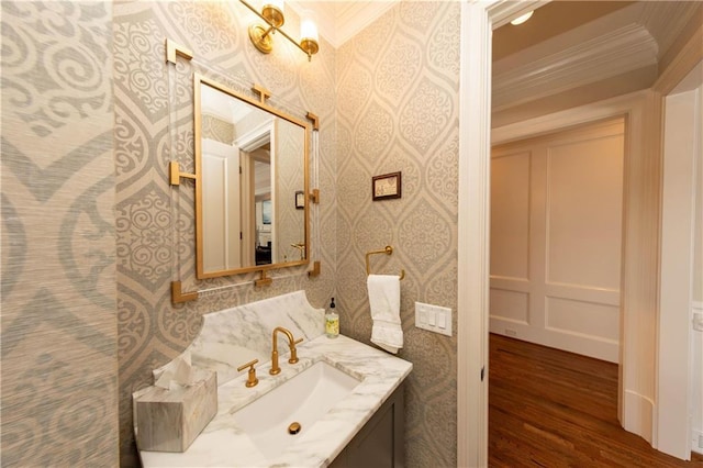 bathroom with vanity, wood finished floors, wallpapered walls, and ornamental molding