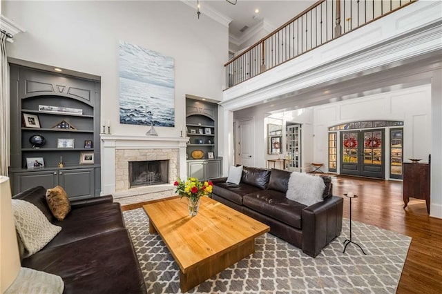 living area with built in shelves, wood finished floors, french doors, a fireplace, and crown molding