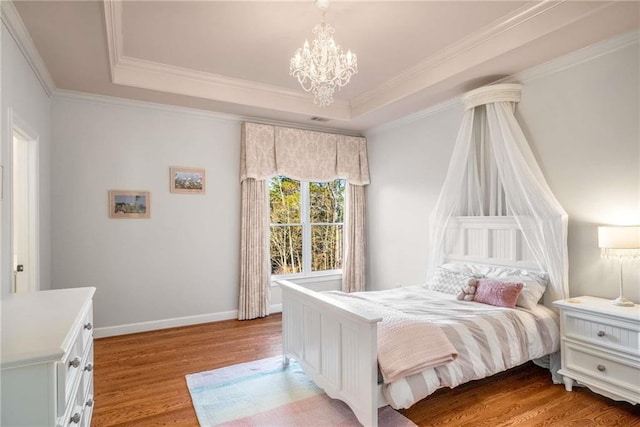 bedroom with an inviting chandelier, a tray ceiling, crown molding, and light wood-style floors