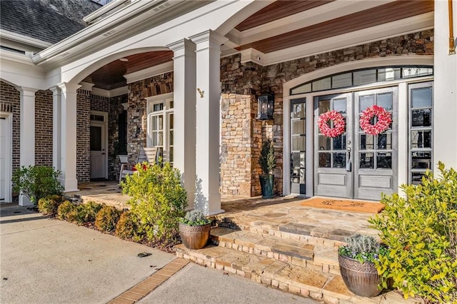 entrance to property with stone siding, brick siding, covered porch, and roof with shingles