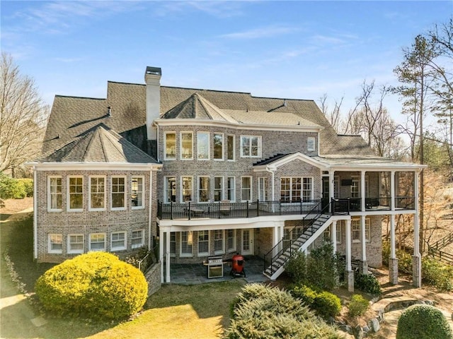 back of house featuring stairs, a sunroom, brick siding, a chimney, and a patio area