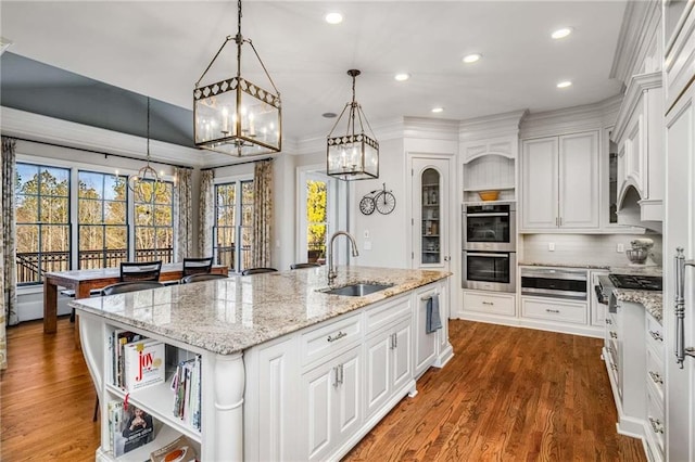 kitchen featuring a sink, a large island with sink, appliances with stainless steel finishes, white cabinetry, and open shelves