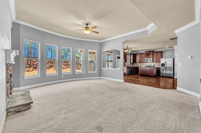 unfurnished living room featuring dark colored carpet, baseboards, crown molding, and ceiling fan with notable chandelier