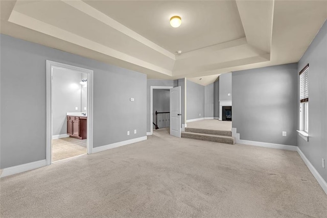unfurnished living room featuring a tray ceiling, baseboards, light carpet, and a fireplace