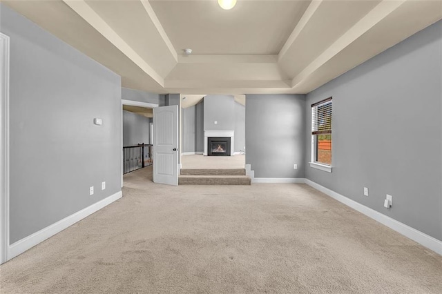 unfurnished living room with carpet, baseboards, a warm lit fireplace, and a raised ceiling