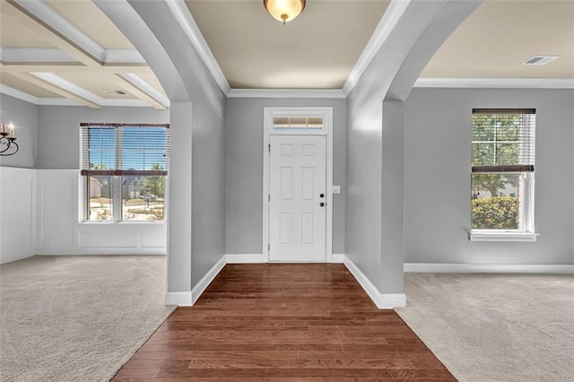 carpeted foyer with visible vents, arched walkways, a chandelier, crown molding, and wood finished floors