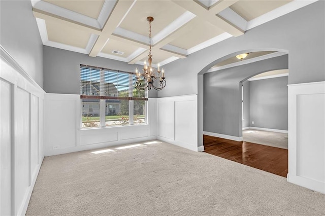 unfurnished dining area with an inviting chandelier, carpet floors, beam ceiling, coffered ceiling, and arched walkways