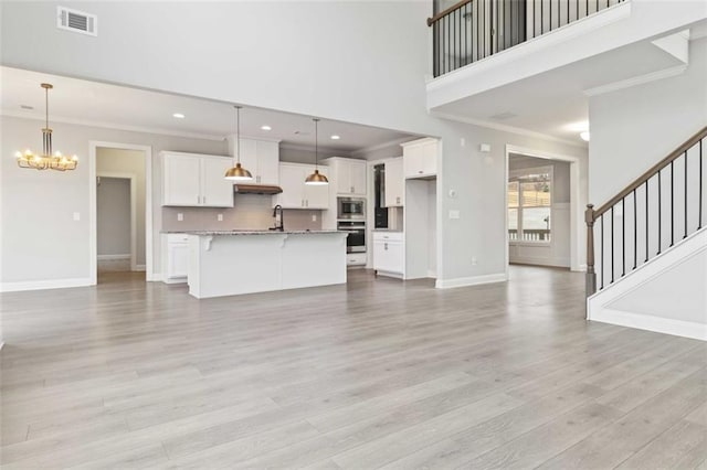 unfurnished living room featuring ornamental molding, a towering ceiling, a chandelier, and light hardwood / wood-style flooring