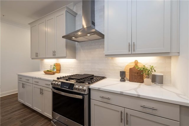 kitchen featuring wall chimney exhaust hood, stainless steel gas range oven, light stone counters, dark wood finished floors, and tasteful backsplash