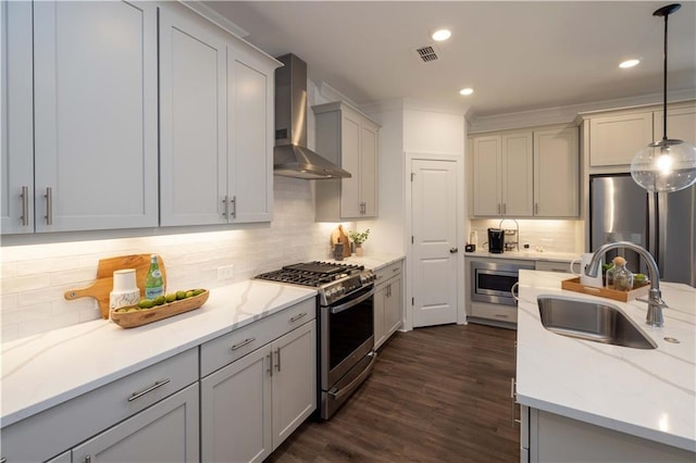 kitchen with stainless steel appliances, wall chimney range hood, a sink, decorative backsplash, and decorative light fixtures