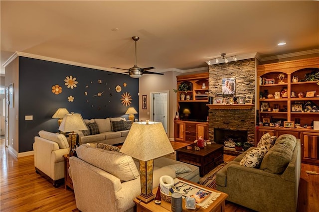 living room featuring ceiling fan, a fireplace, crown molding, light hardwood / wood-style flooring, and built in shelves