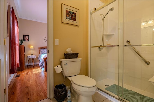 bathroom with a shower with shower door, hardwood / wood-style flooring, toilet, and ornamental molding