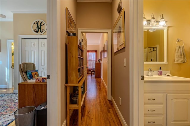 corridor featuring sink, crown molding, and light hardwood / wood-style floors