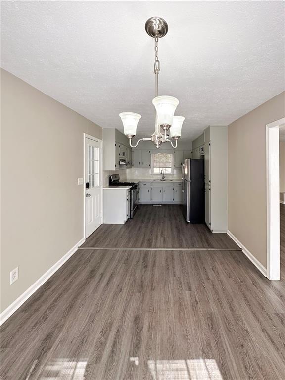 unfurnished living room featuring dark hardwood / wood-style flooring, sink, an inviting chandelier, and a textured ceiling