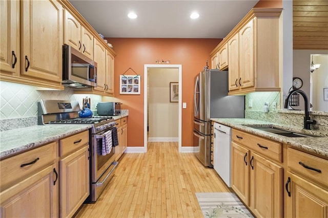 kitchen featuring light stone countertops, appliances with stainless steel finishes, sink, and light wood-type flooring