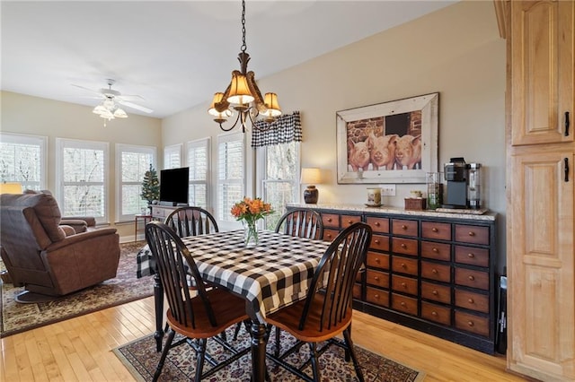 dining space with ceiling fan with notable chandelier and light hardwood / wood-style flooring