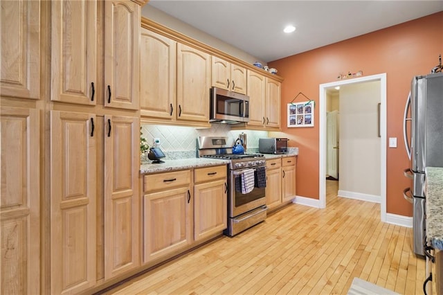 kitchen featuring light hardwood / wood-style flooring, appliances with stainless steel finishes, tasteful backsplash, light stone countertops, and light brown cabinetry