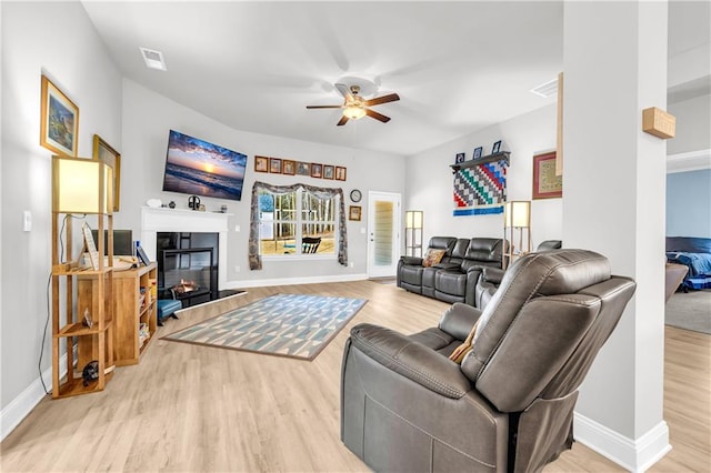 living area featuring visible vents, ceiling fan, baseboards, wood finished floors, and a glass covered fireplace