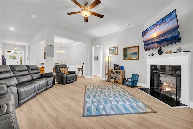 living area with a glass covered fireplace, wood finished floors, visible vents, and baseboards