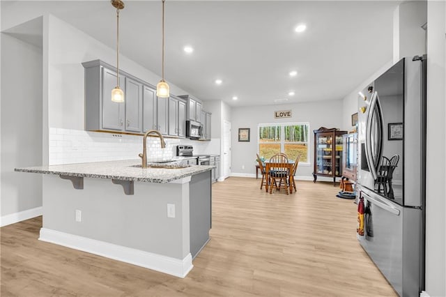 kitchen with gray cabinets, a sink, a kitchen breakfast bar, stainless steel appliances, and a peninsula