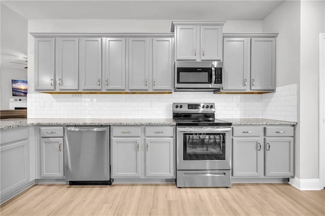 kitchen with gray cabinetry, tasteful backsplash, stainless steel appliances, light wood finished floors, and light stone countertops