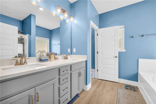 bathroom featuring a garden tub, wood finished floors, double vanity, and a sink