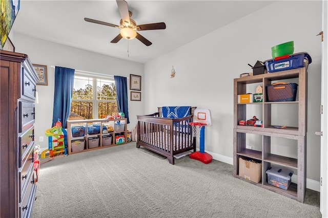 carpeted bedroom with a crib, baseboards, and a ceiling fan