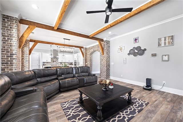 living area featuring arched walkways, brick wall, wood finished floors, baseboards, and beam ceiling