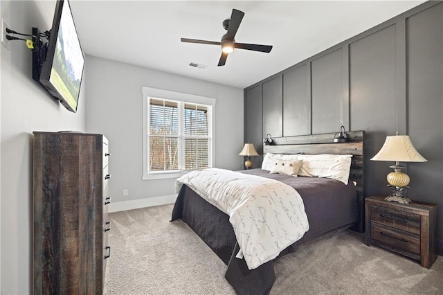 bedroom with ceiling fan, a decorative wall, light colored carpet, visible vents, and baseboards