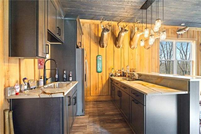 kitchen with freestanding refrigerator, light countertops, wood walls, pendant lighting, and a sink