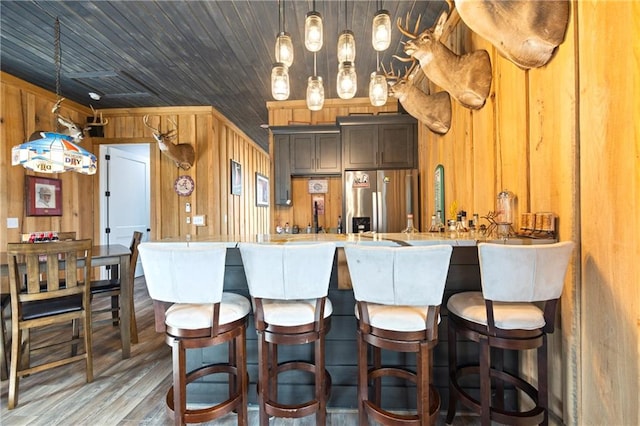 kitchen with stainless steel fridge with ice dispenser, wood finished floors, hanging light fixtures, light countertops, and wood walls