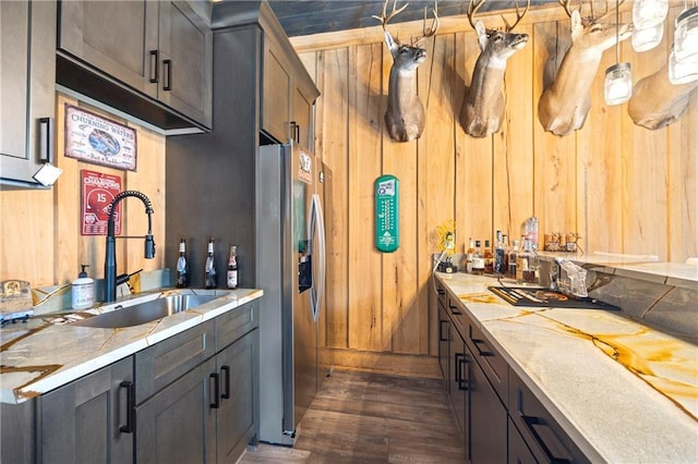 kitchen with dark wood-style flooring, pendant lighting, a sink, wooden walls, and stainless steel fridge with ice dispenser